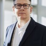 Profile portrait of a confident business executive wearing eyeglasses in a sunlit office setting.